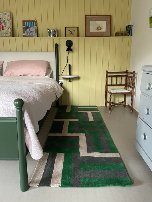 Bedroom with green geometric rug, wooden chair, and shelves with decor items.