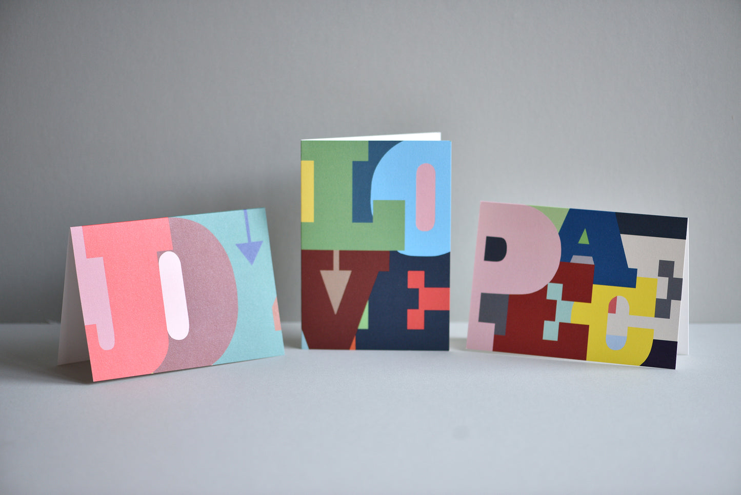 Three colorful greeting cards with letter designs on a gray background