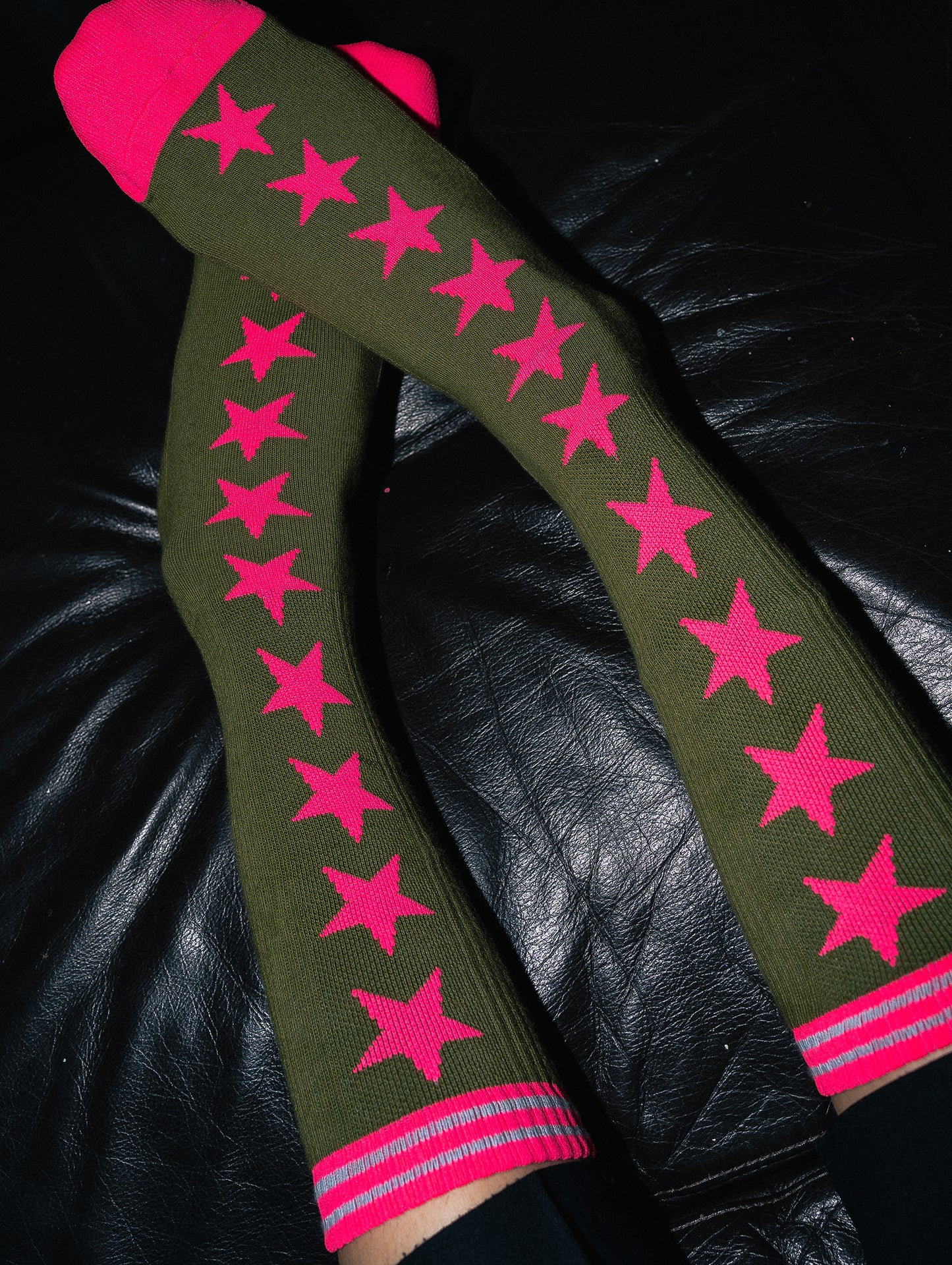 Green knee-high socks with pink stars on a black leather surface