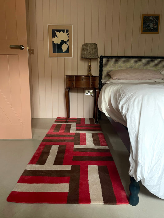 Bedroom with a patterned red and brown rug, bed, and side table.