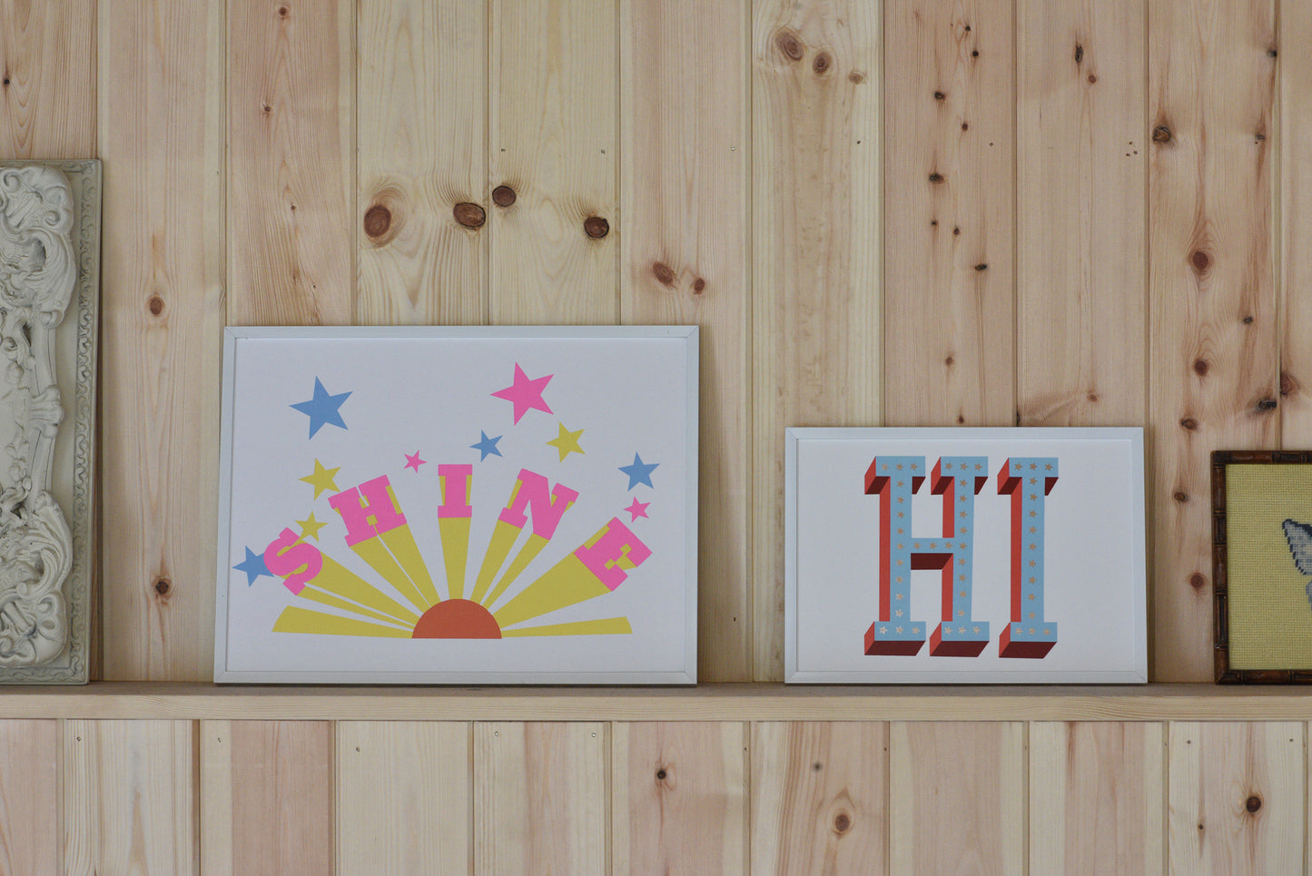 Two framed decorative signs on a wooden shelf with a wooden wall background.