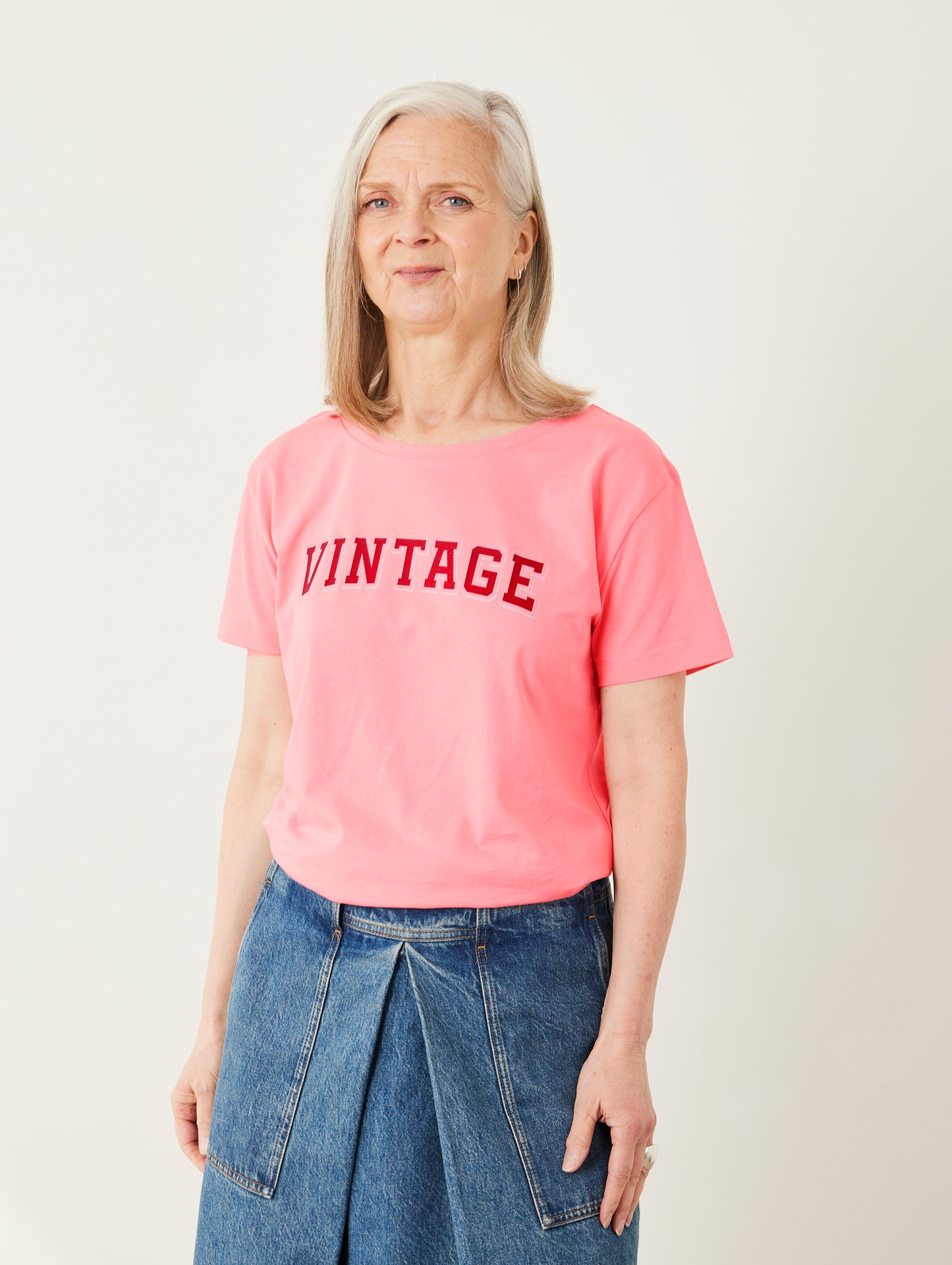 Woman wearing a pink 'VINTAGE' t-shirt and blue jeans on a white background