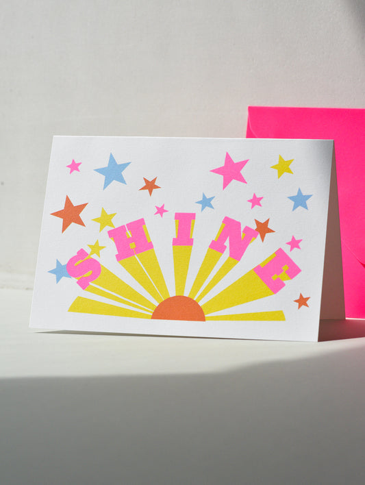 Colorful 'SHINE' card with stars on a white surface