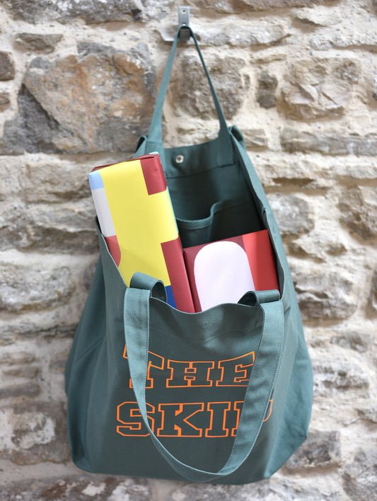 Green tote bag with colorful items against a stone wall
