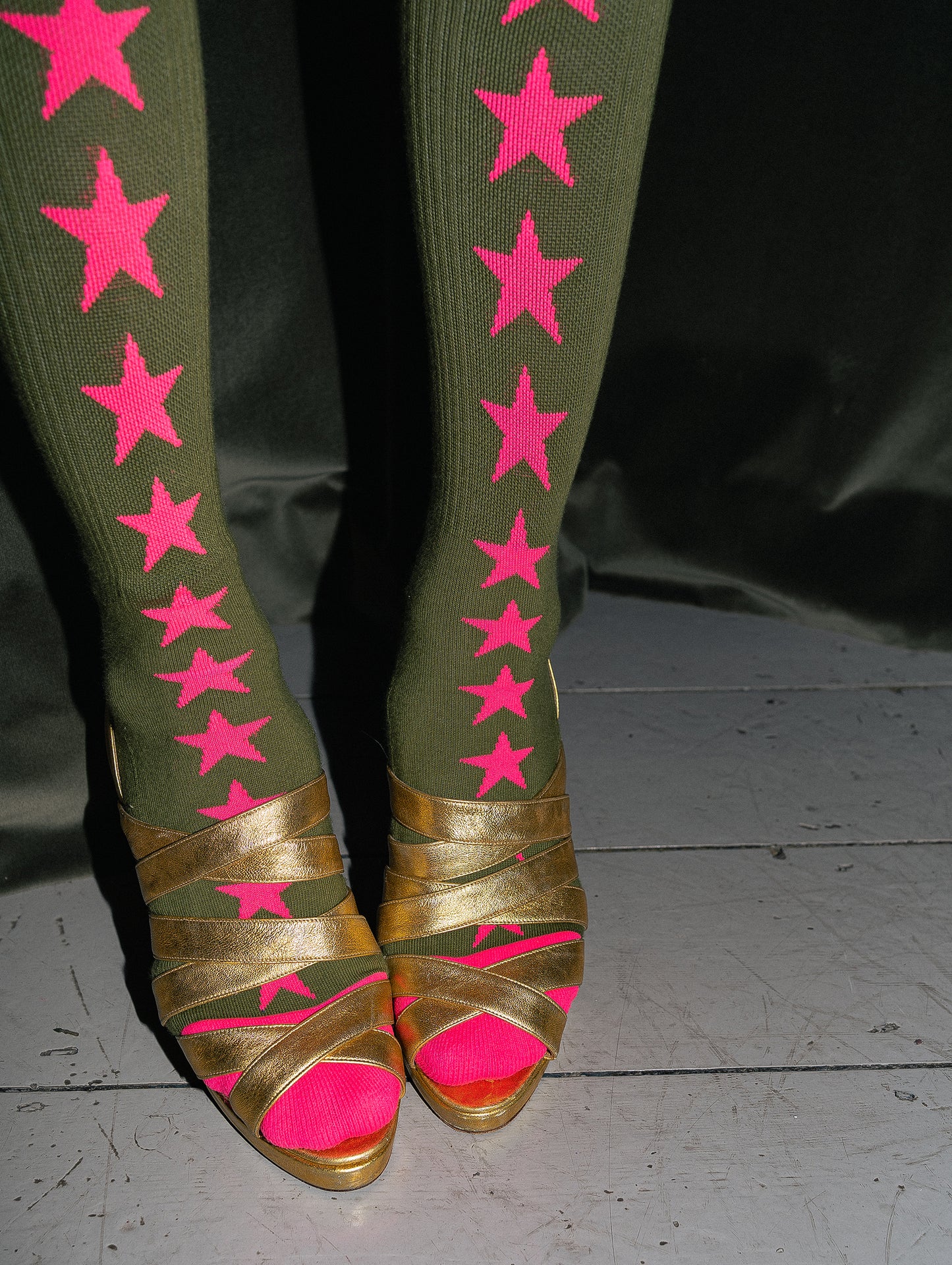 Green leggings with pink stars and gold sandals with pink soles on a dark background