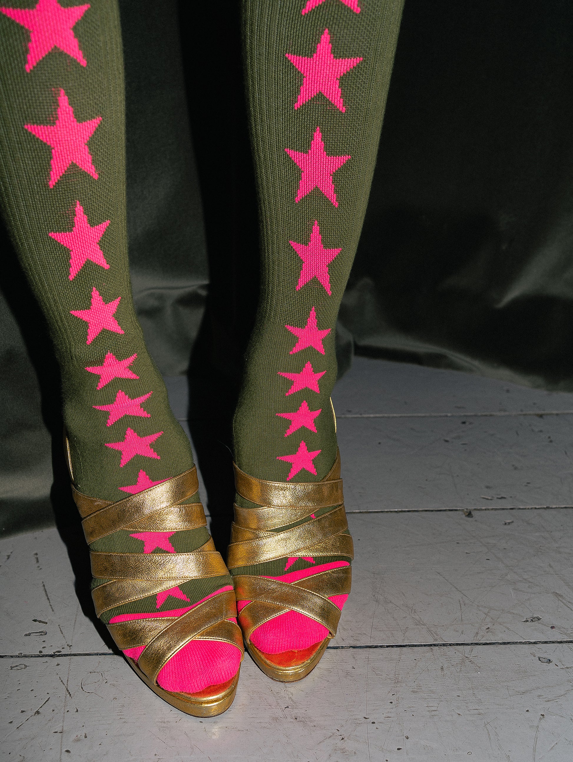 Green leggings with pink stars and gold sandals with pink soles on a dark background