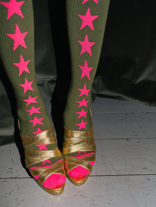 Green leggings with pink stars and gold sandals with pink soles on a dark background