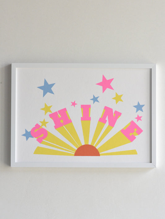 Framed artwork with 'SHINE' text and colorful stars on a white background