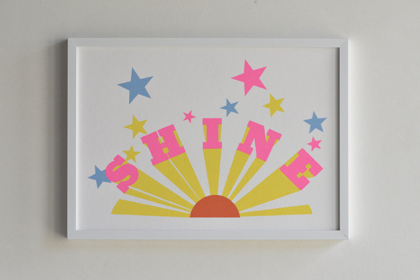 Framed artwork with the word 'SHINE' in bright colors on a gray background