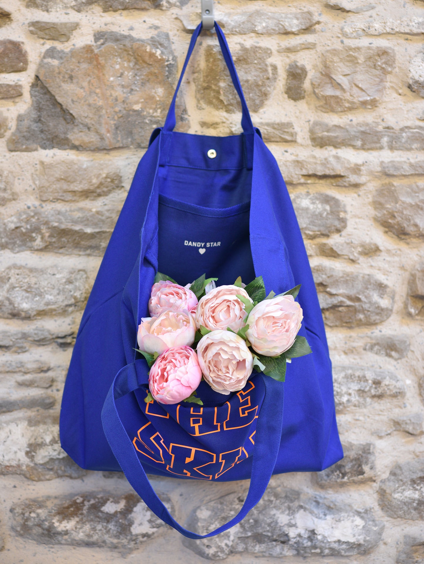 Blue tote bag with floral arrangement against a stone wall