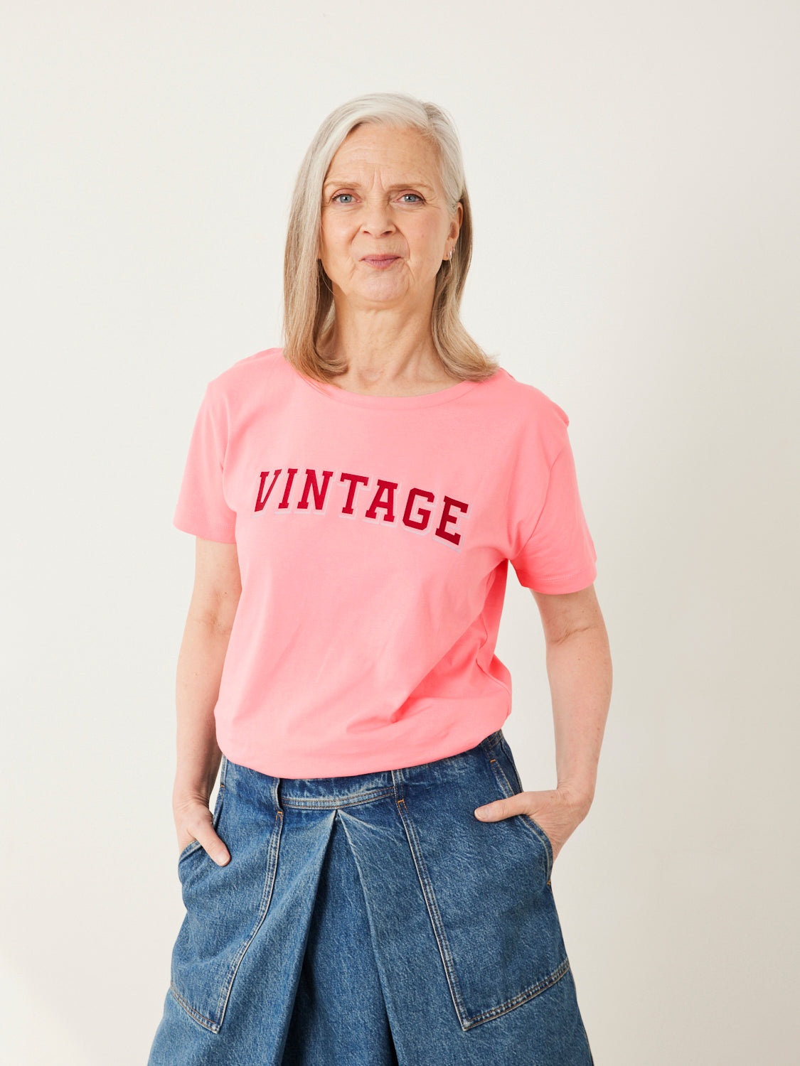 Person wearing a pink 'VINTAGE' t-shirt and blue jeans on a plain background