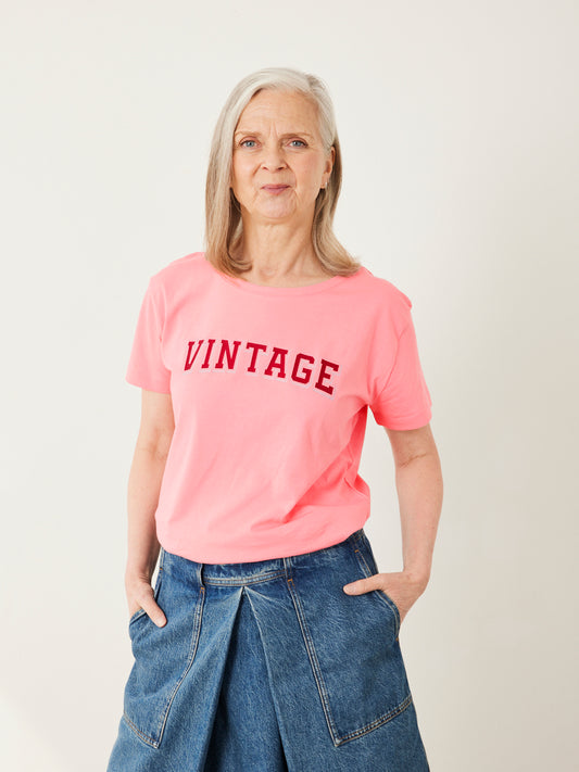 Person wearing a pink 'VINTAGE' t-shirt and blue jeans on a plain background