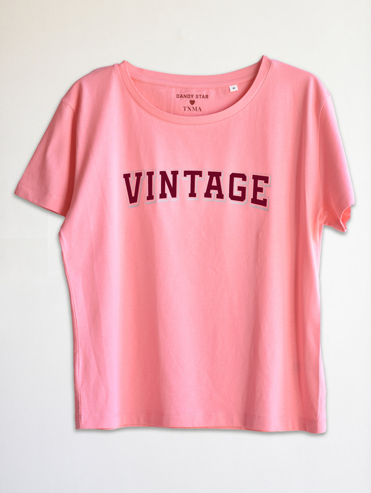 A pink short-sleeve t-shirt with the word 'VINTAGE' printed across the chest in a dark red arched font, displayed against a plain off-white background.