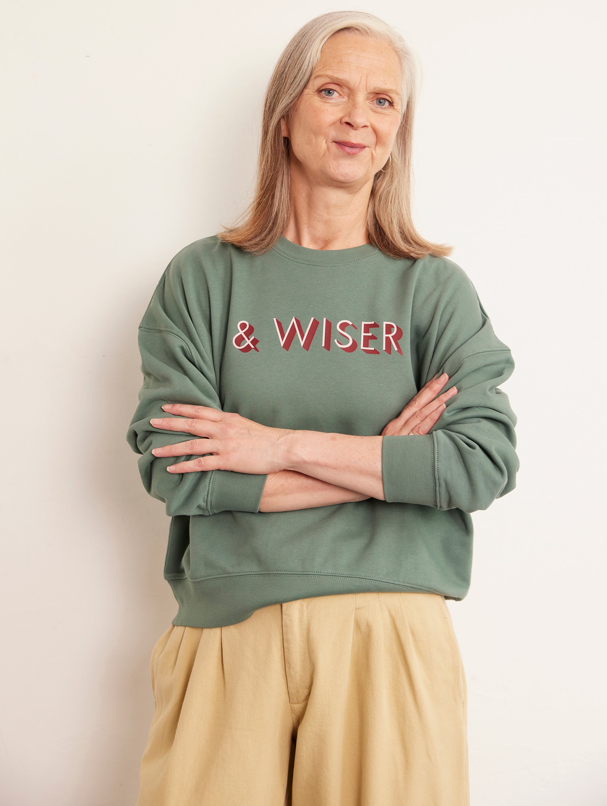 Person wearing a green sweatshirt with 'WISER' text, standing against a plain background