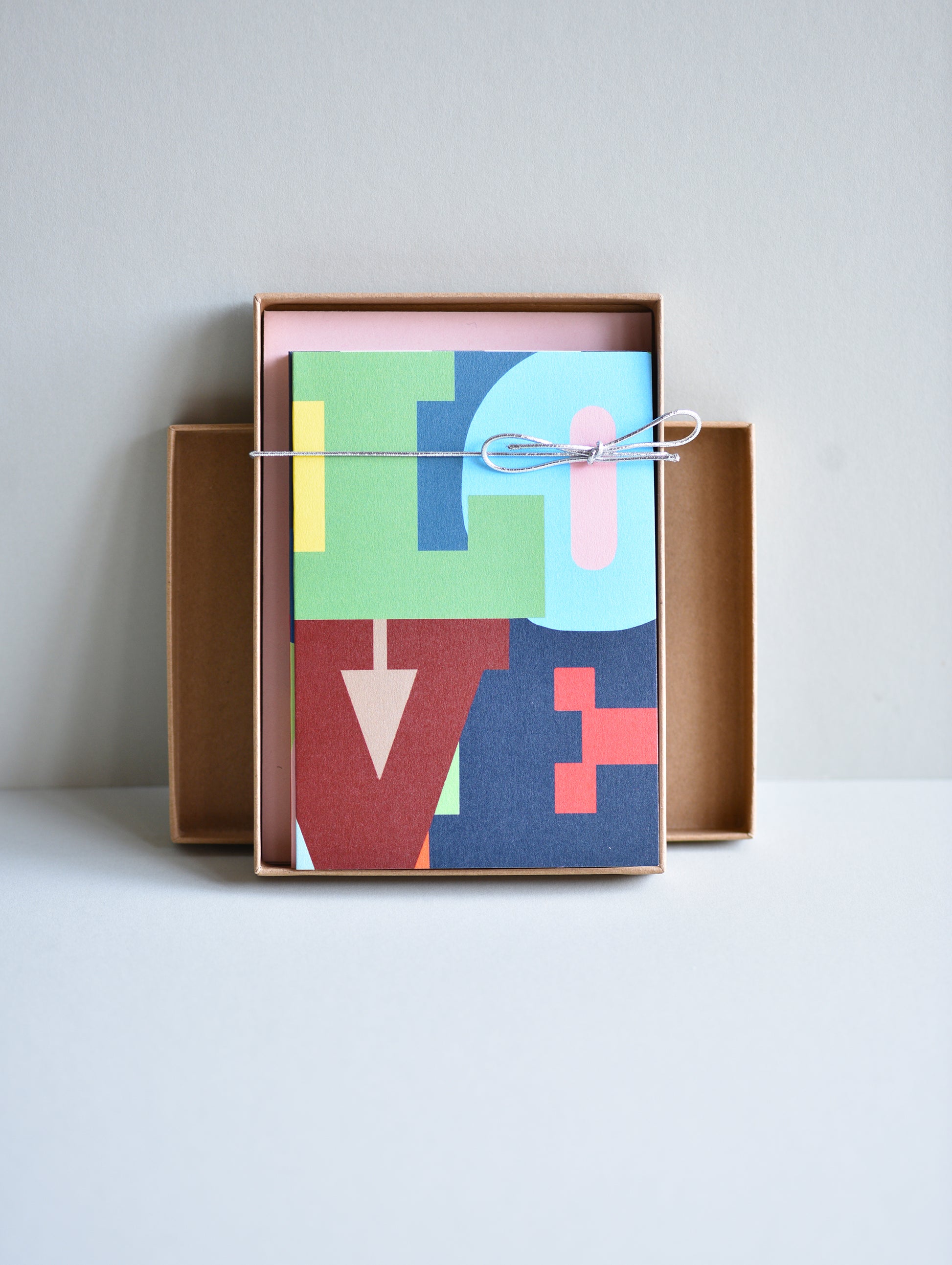 Colorful geometric-patterned notebook in a cardboard box on a light gray background