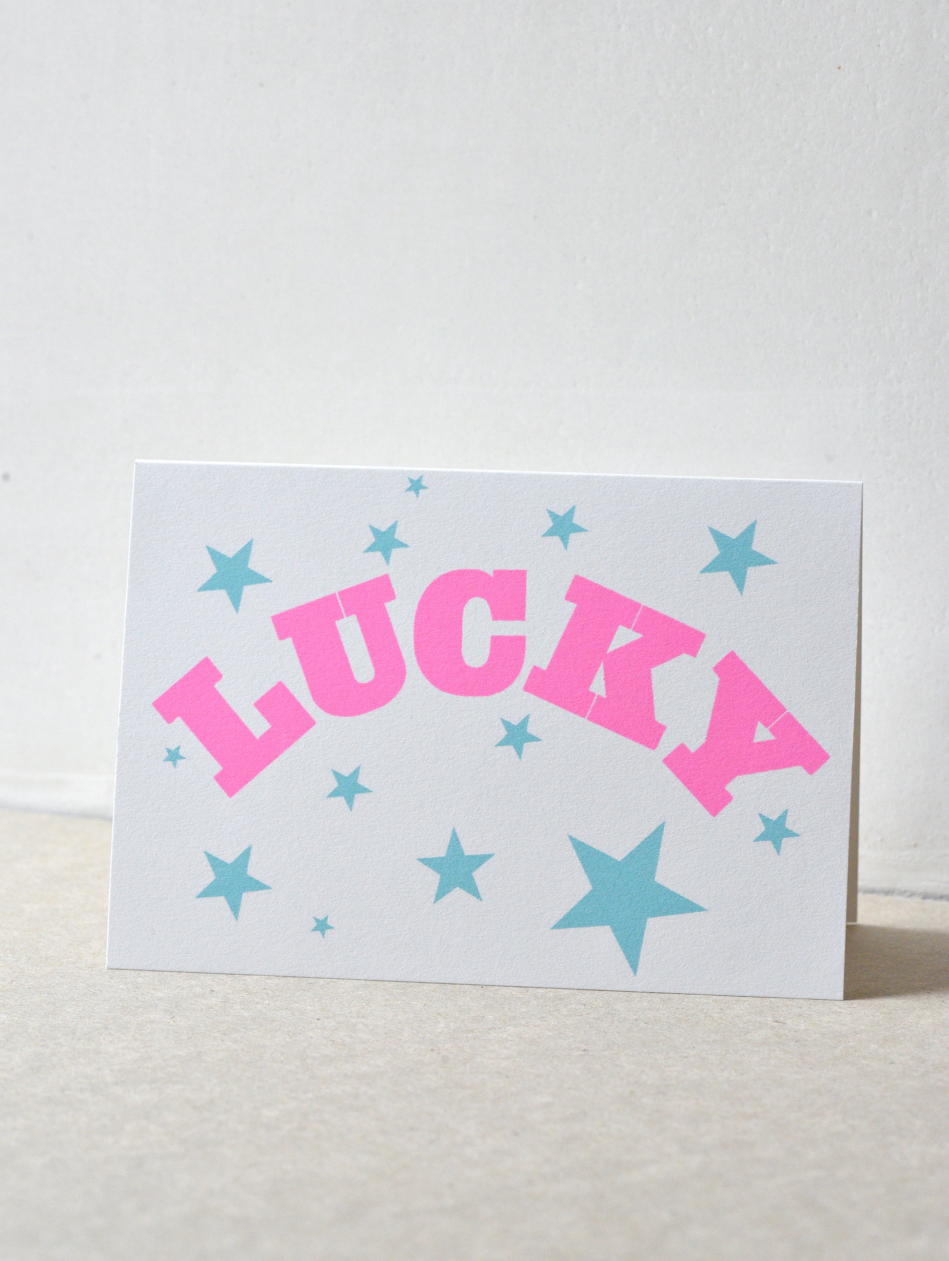 Card with 'LUCKY' in pink and stars in blue on a light gray background