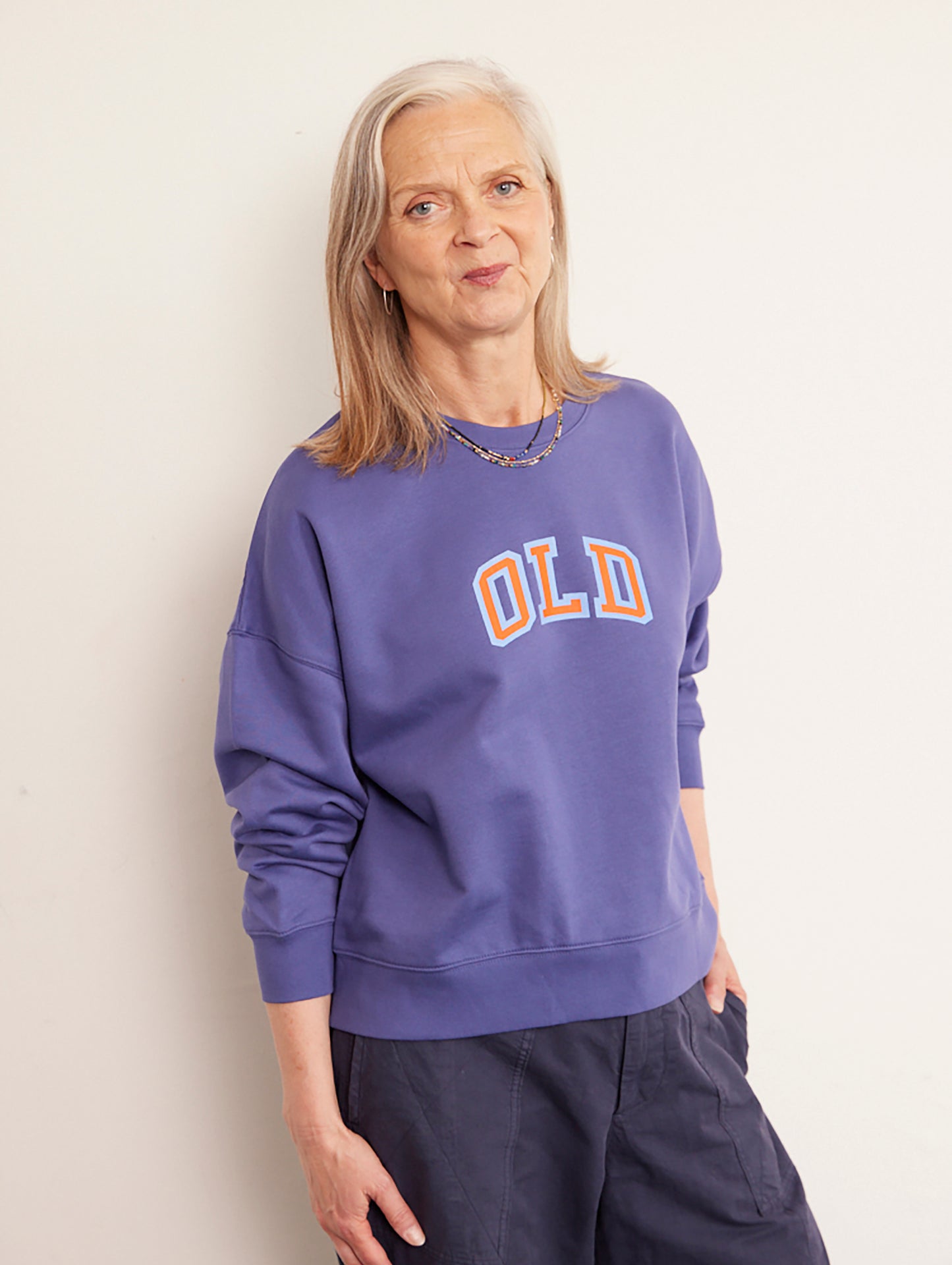 Alyson Walsh wearing a purple sweatshirt with 'OLD' printed on it against a plain background