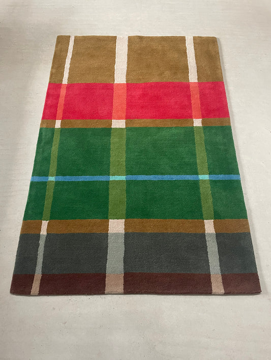 Plaid patterned rug with red, green, brown, and blue colors on a plain background