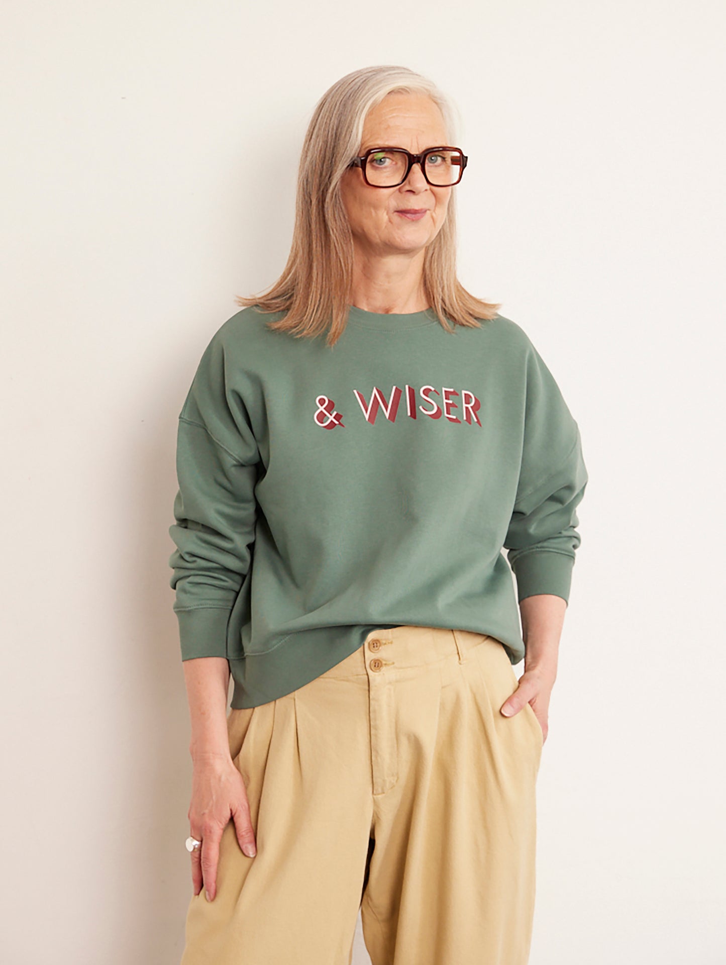 Alyson Walsh wearing a green sweatshirt with 'WISER' text, standing against a plain background