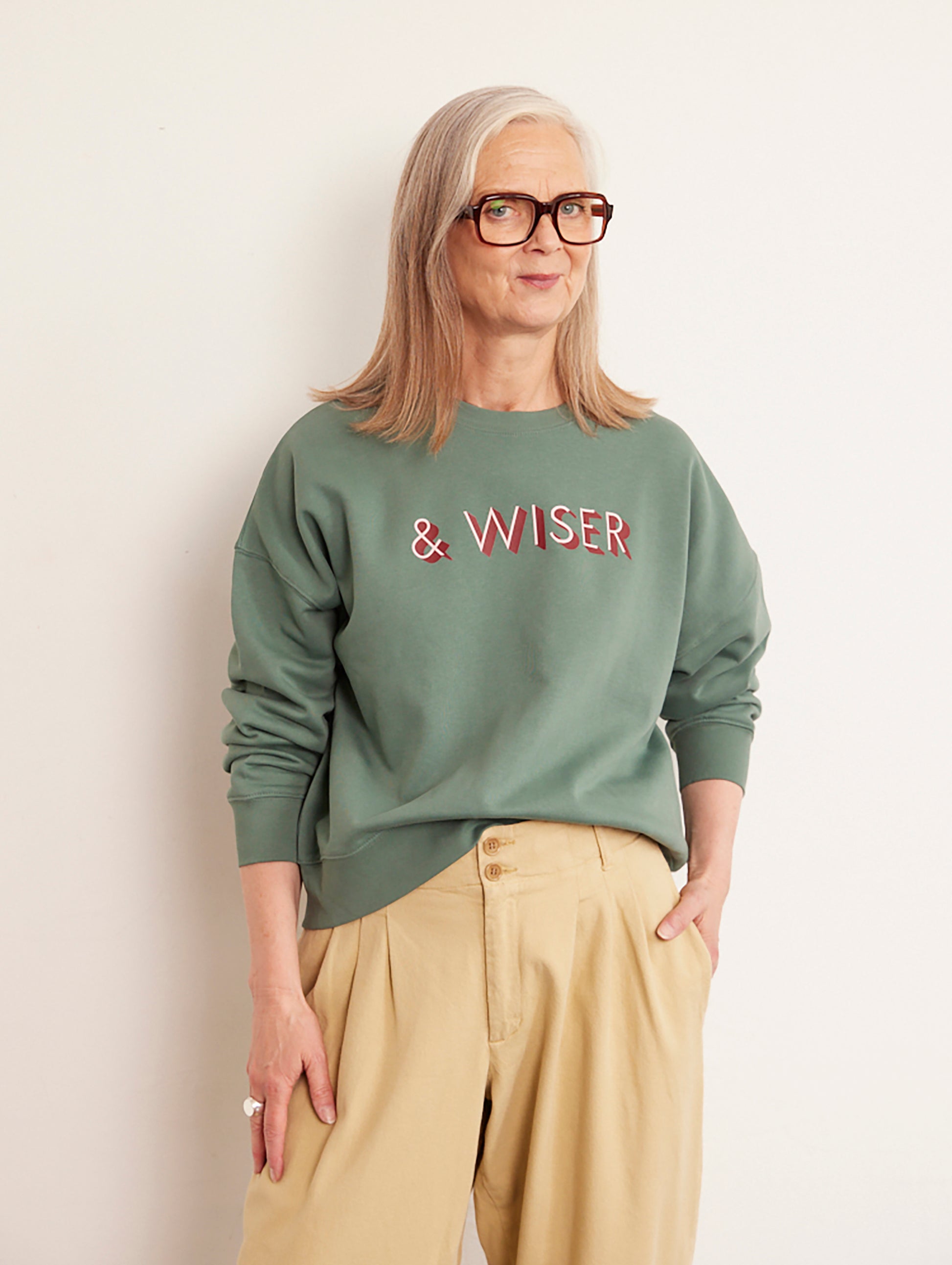 Alyson Walsh wearing a green sweatshirt with 'WISER' text, standing against a plain background